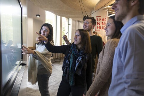 Un groupe d'étudiants pointant sur un écran. Tous les étudiants sont souriants. Image pour le parcours d'engagement citoyen étudiant.